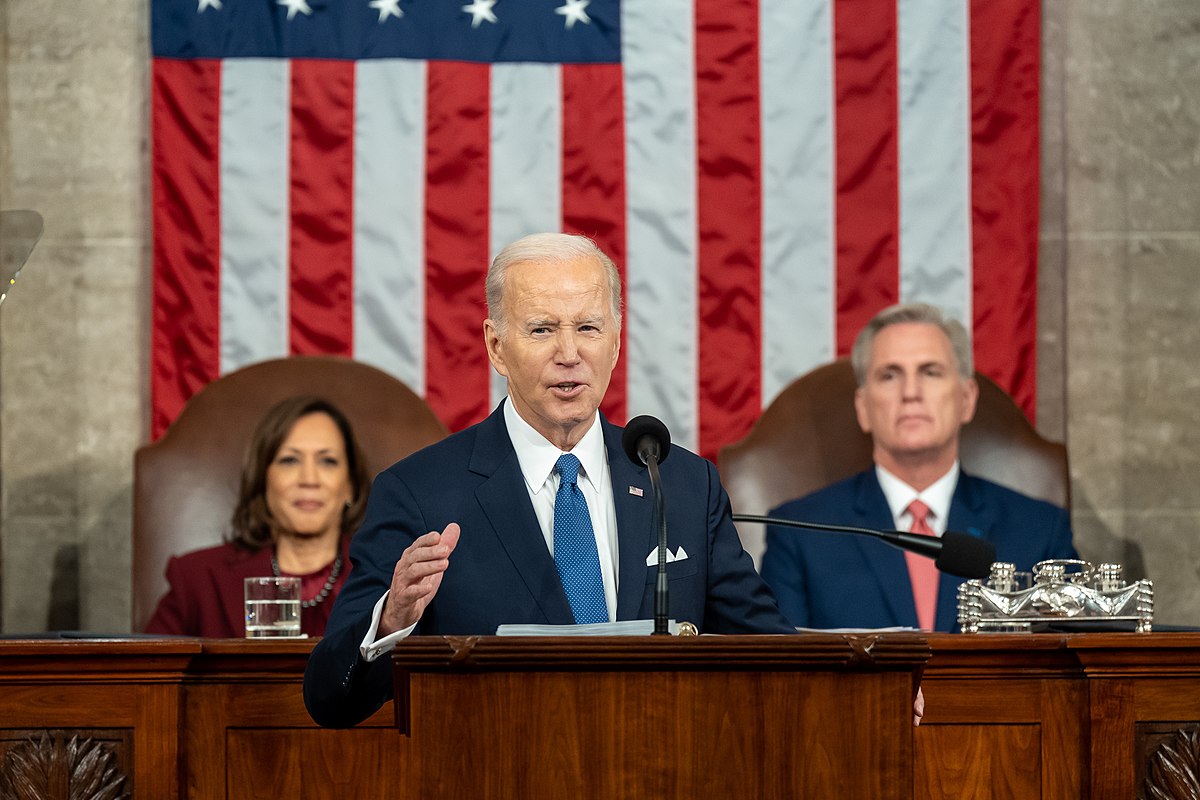 Photo of President Biden delivering the State of the Union address with Vice President Kamala Harris and Speaker Kevin McCarthy seated behind him.